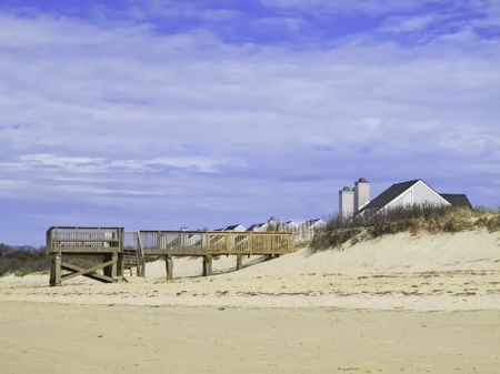 Coastal landscape: Beach view of boardwalk and deck by dune near peaked roofs of houses in Cape Cod, Massachusetts