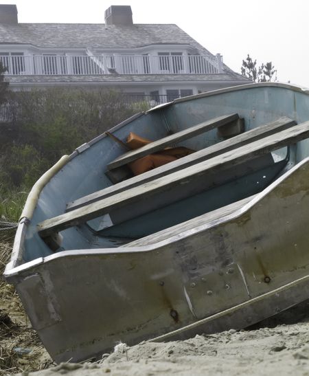 Vacant rowboat beached near house in Cape Cod on misty afternoon (selective focus)