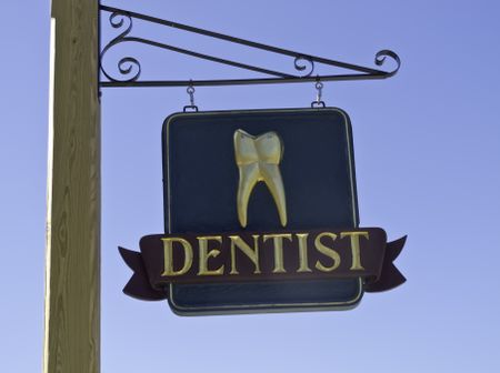Dentist's sign with gold tooth against a blue sky