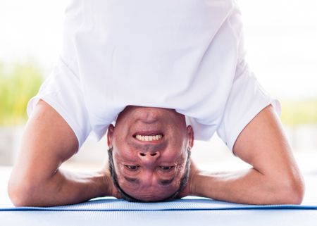 Happy man headstanding while doing yoga exercises