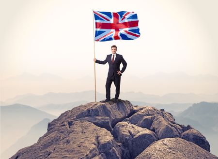 Successful businessman on the top of a mountain holding victory flag