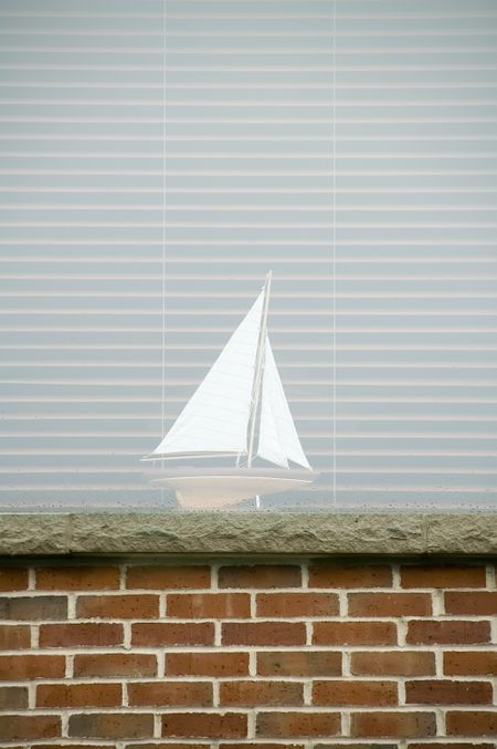 Model sailboat inside wet window with blinds