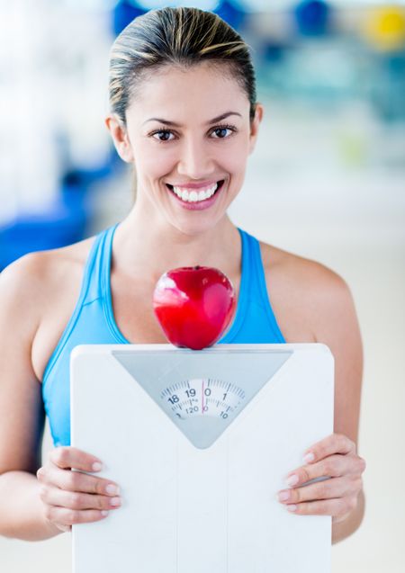 Beautiful woman dieting holding a weight scale and an apple