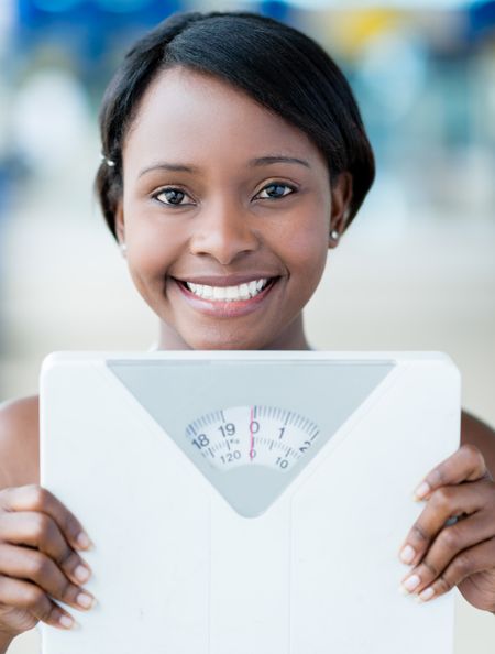 Happy woman at the gym holding weight scale