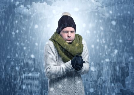 Young man freezing in warm clothing with city concept