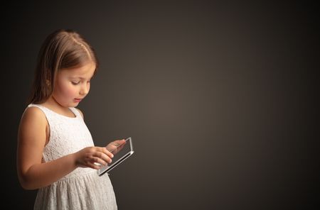 Adorable little girl using tablet with dark empty space
