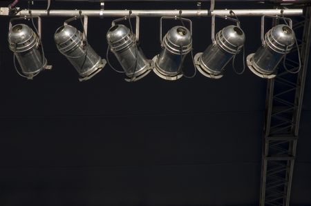 Six stage lights hanging in sunlight by dark wall and ladder