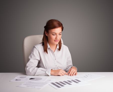 Beautiful young businesswoman sitting at desk and doing paperwork