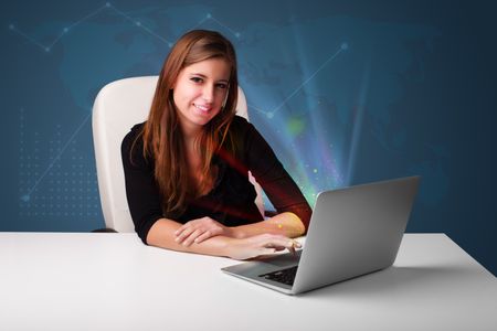 Beautiful young woman sitting at desk and typing on laptop with abstract lights