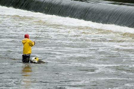 Woman in waders and yellow raincoat fishing near dam in river