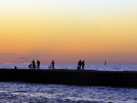 Twilight silhouettes on a summer evening: Unidentifiable couple and bicyclists returning to shore after watching sunset over Lake Michigan from a jetty in South Haven, Michigan