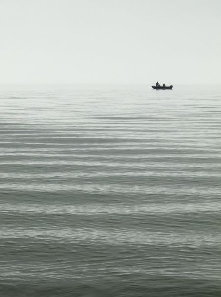 Three unidentifiable fishermen in small boat on Lake Michigan on an overcast day