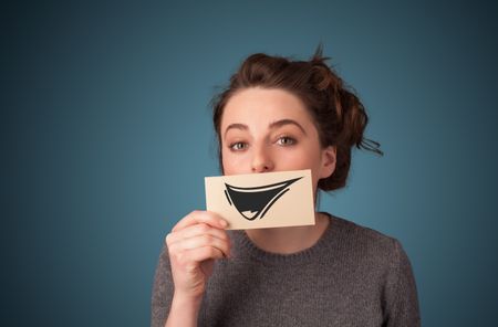 Happy cute girl holding paper with funny smiley drawing on gradient background