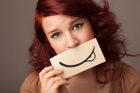 Pretty young girl holding white card with smile drawing on gradient background