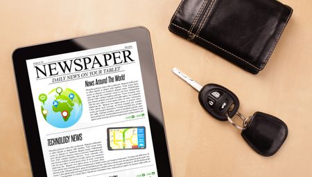 Workplace with tablet pc showing news and a cup of coffee on a wooden work table close-up