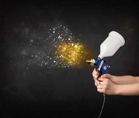 Worker with airbrush painting with glowing golden paint and particles