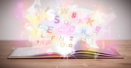Open book with glowing letters on concrete background. Colorful education concept