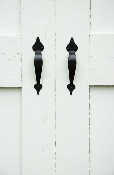 Two black iron handles with a few raindrops on white wooden doors