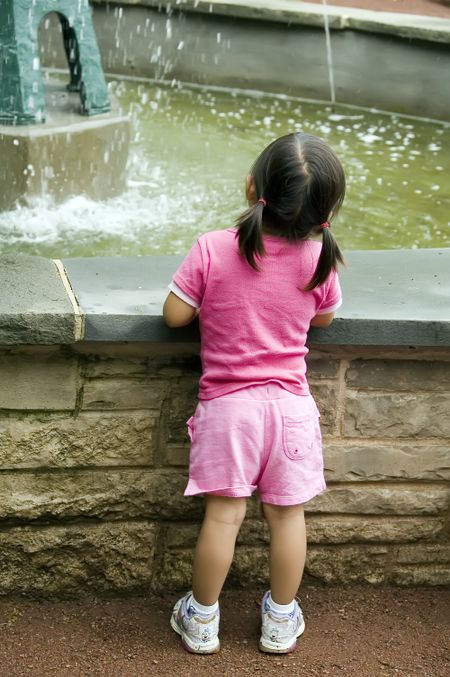 Little girl by stone wall watching water fall from fountain