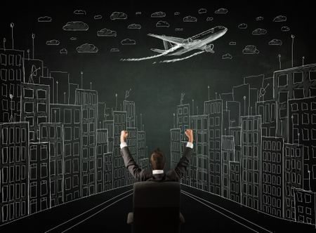 Young businessman sitting in an office chair and looking on a sketched cityscape drawing on a chalkboard