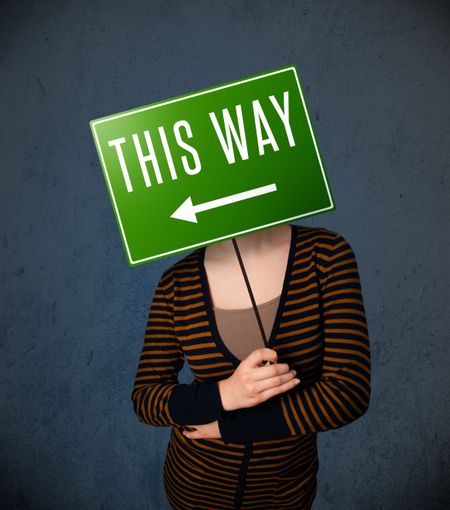 Young lady standing and holding a green direction sign in front of her head