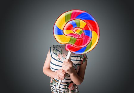 Young lady holding a colorful striped lollipop in front of her head