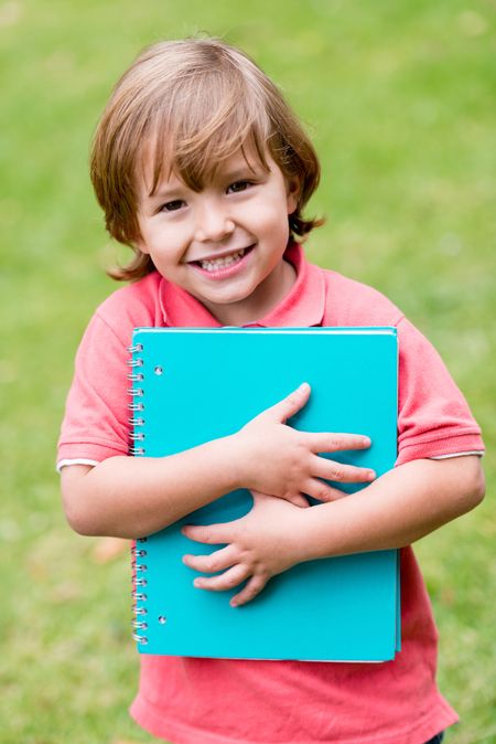Beautiful school boy looking very happy holding a notebook