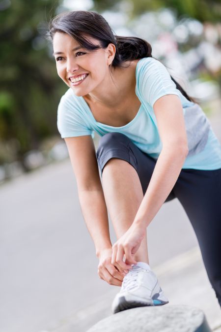 Happy female runner tying her shoelace outdoors 
