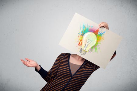 Woman holding a cardboard with coloured paint splashes and lightbulb concept in front of her head