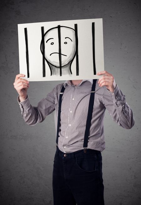 Businessman holding a paper with a prisoner in jail behind the bars on it in front of his head