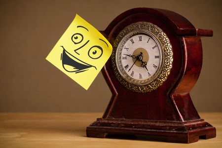 Drawn smiley face on a post-it note sticked on a clock
