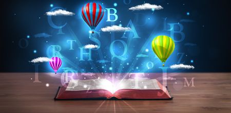 Open book with glowing fantasy abstract clouds and balloons on wood deck