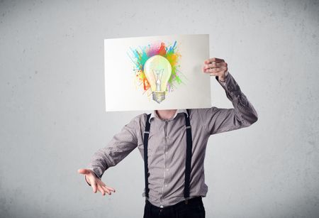 Businessman holding a cardboard with colored paint splashes and lightbulb in front of his head