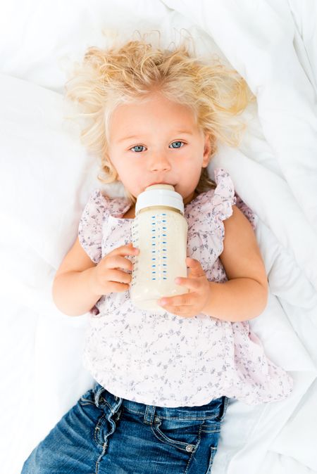Cute baby girl drinking from a bottle in bed 