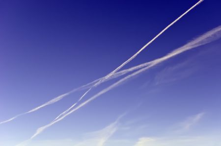 Travel concept of intersecting journeys: Three contrails crisscrossing while another dissipates across blue sky