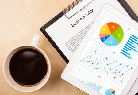 Workplace with tablet pc showing charts and a cup of coffee on a wooden work table close-up