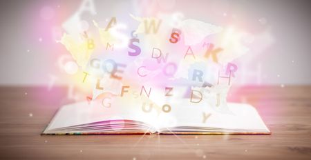 Open book with glowing letters on concrete background. Colorful education concept