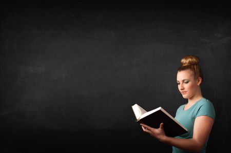 Young lady reading a book in front of a blackboard 