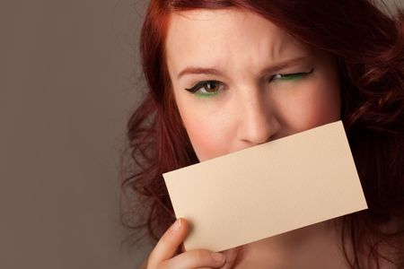 Cute girl holding white card at front of her lips with copy space on gradient background