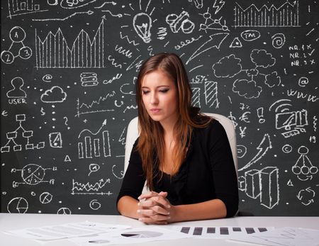 Pretty young businesswoman sitting at desk with business scheme and icons