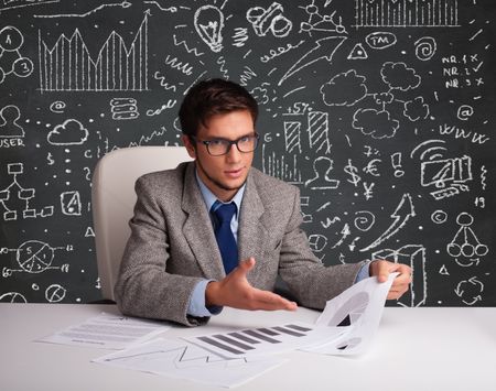 Young businessman sitting at desk with business scheme and icons