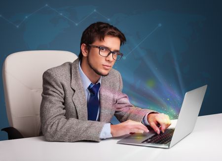 Handsome young man sitting at desk and typing on laptop with abstract lights