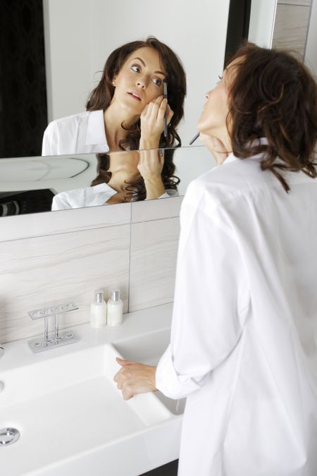 Attractive young woman doing her makeup in front of the bathroom mirror.