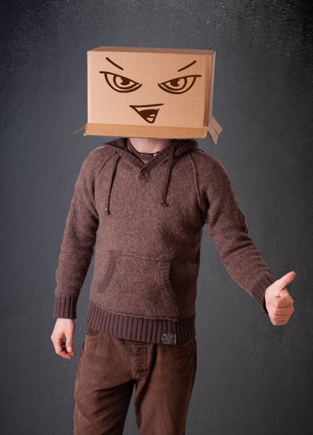 Young man standing and gesturing with a cardboard box on his head with evil face