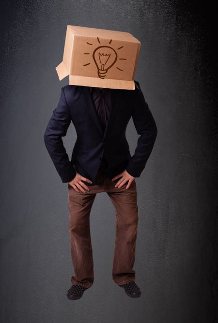 Young man standing and gesturing with a cardboard box on his head with light bulb