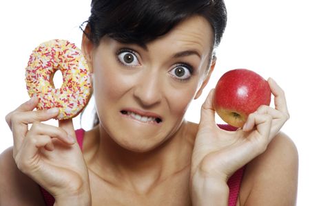 Young woman deciding between an apple or doughnut.