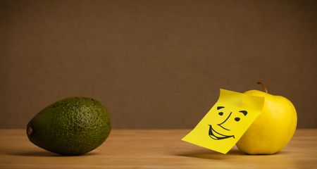 Apple with sticky post-it note looking at avocado