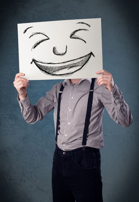 Businessman holding a paper with a drawed smiley face on it in front of his head