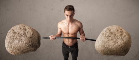 Strong muscular man lifting large rock stone weights
