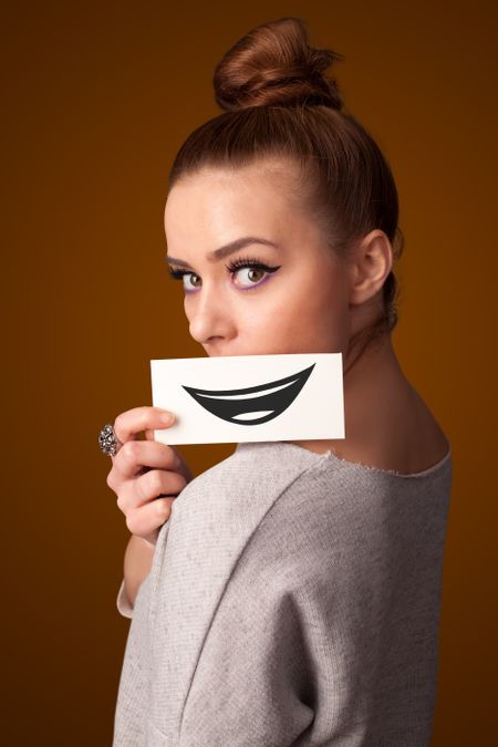 Happy pretty woman holding card with funny smiley on gradient background